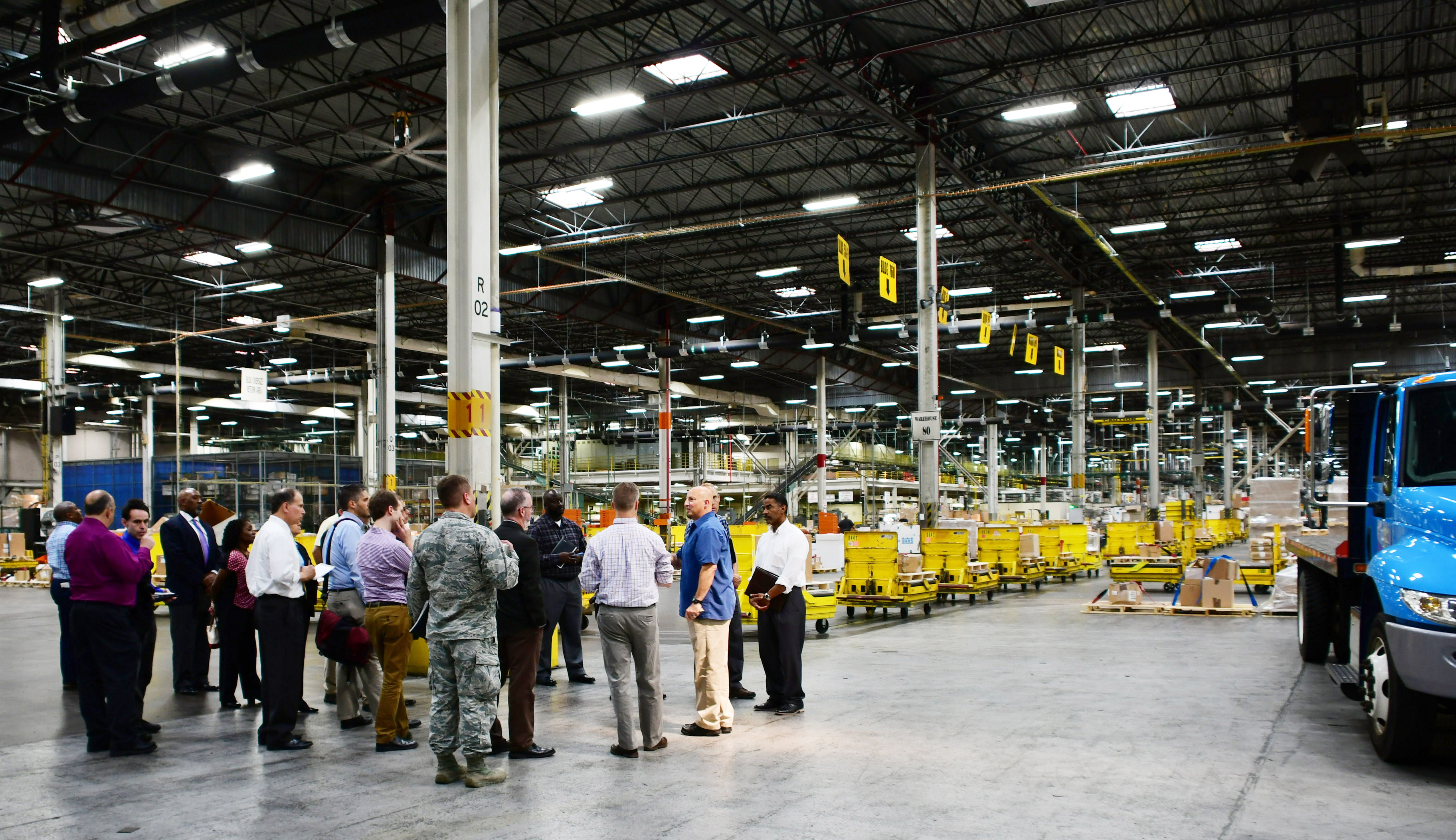 A group is gathered in a warehouse, showing the expanse of the warehouse behind them